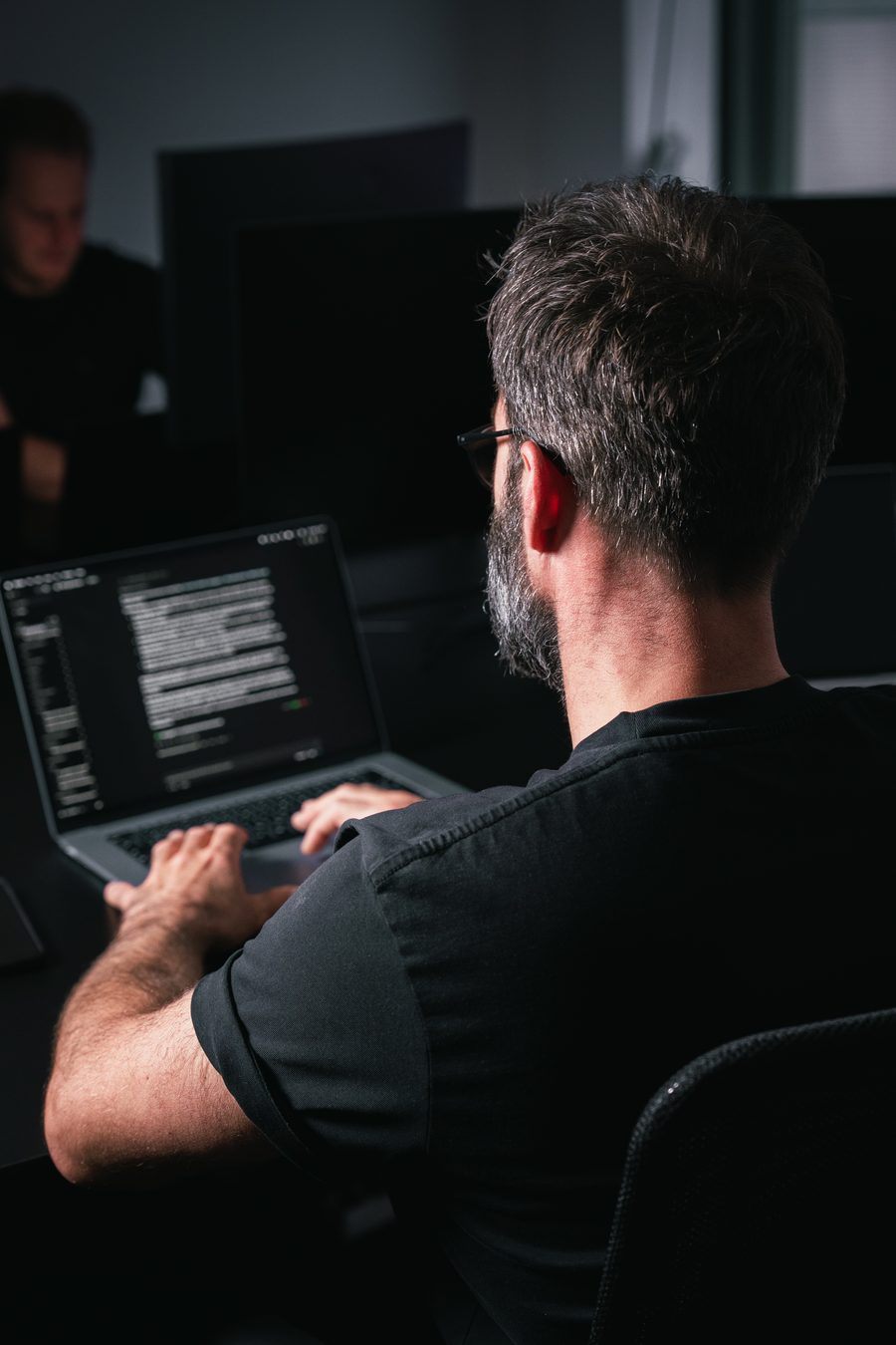 Ivo Klink van achteren in een donkere ruimte, met code op het scherm van zijn laptop