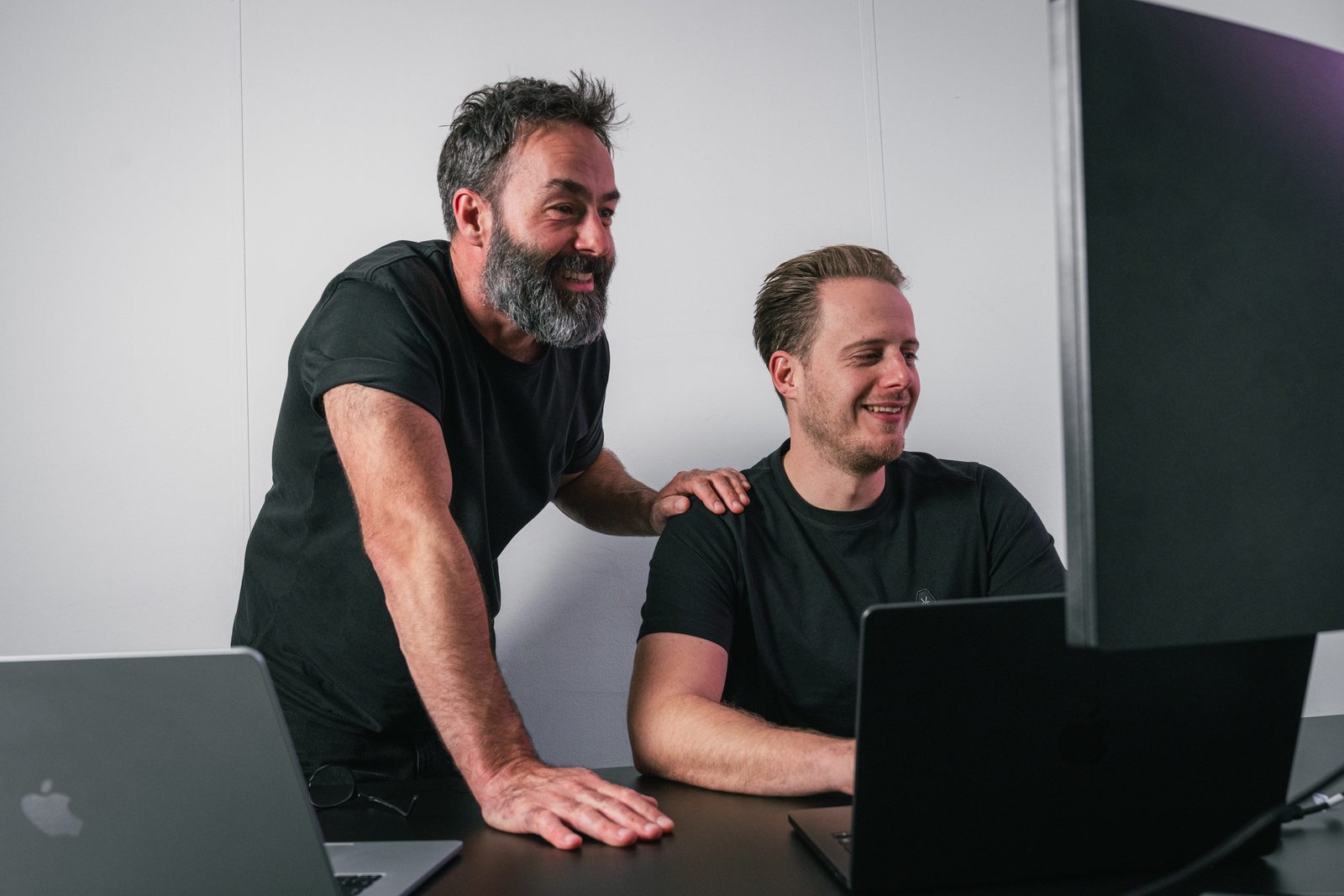 Ivo Klink staat met een hand op de schouder van Maurits den Dunnen, allebei lachend naar het scherm van een laptop
